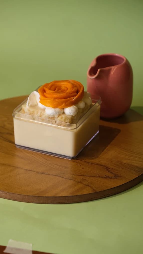 A mango tres leches dessert topped with a mango rose, on a wooden board