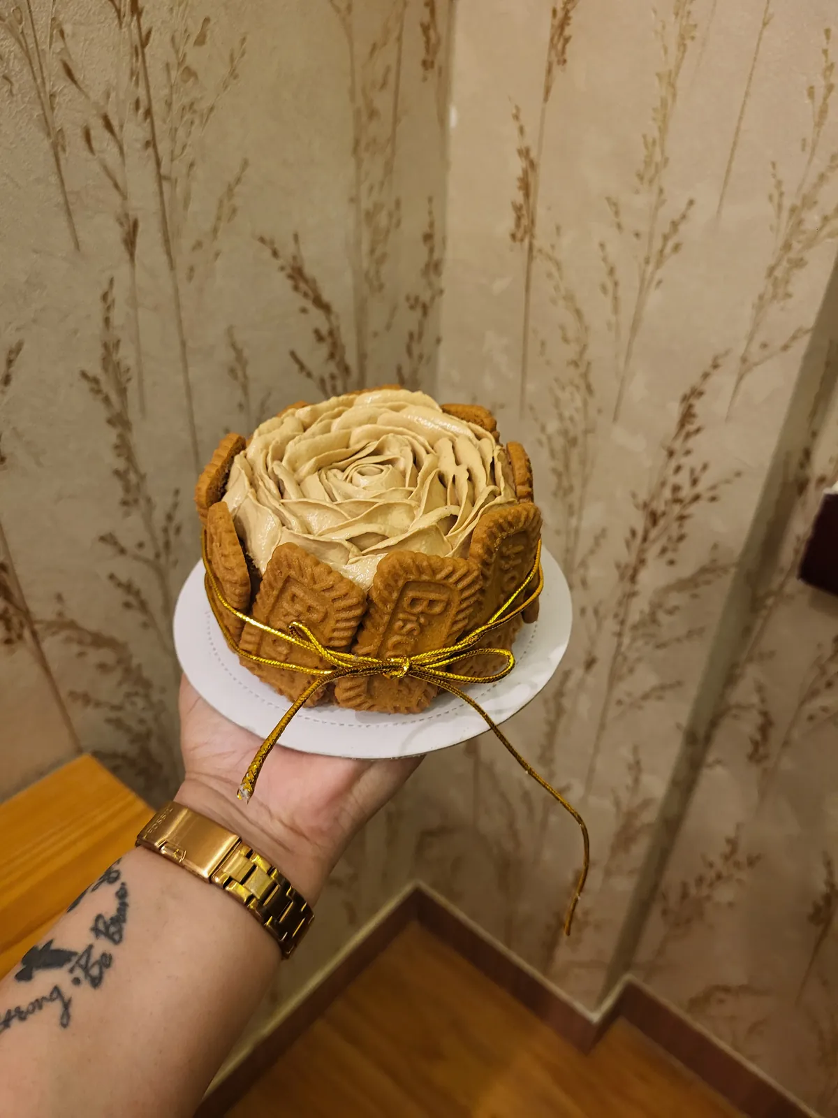 A Biscoff cake — a piped buttercream rosette ringed with Biscoff biscuits and tied with a gold ribbon