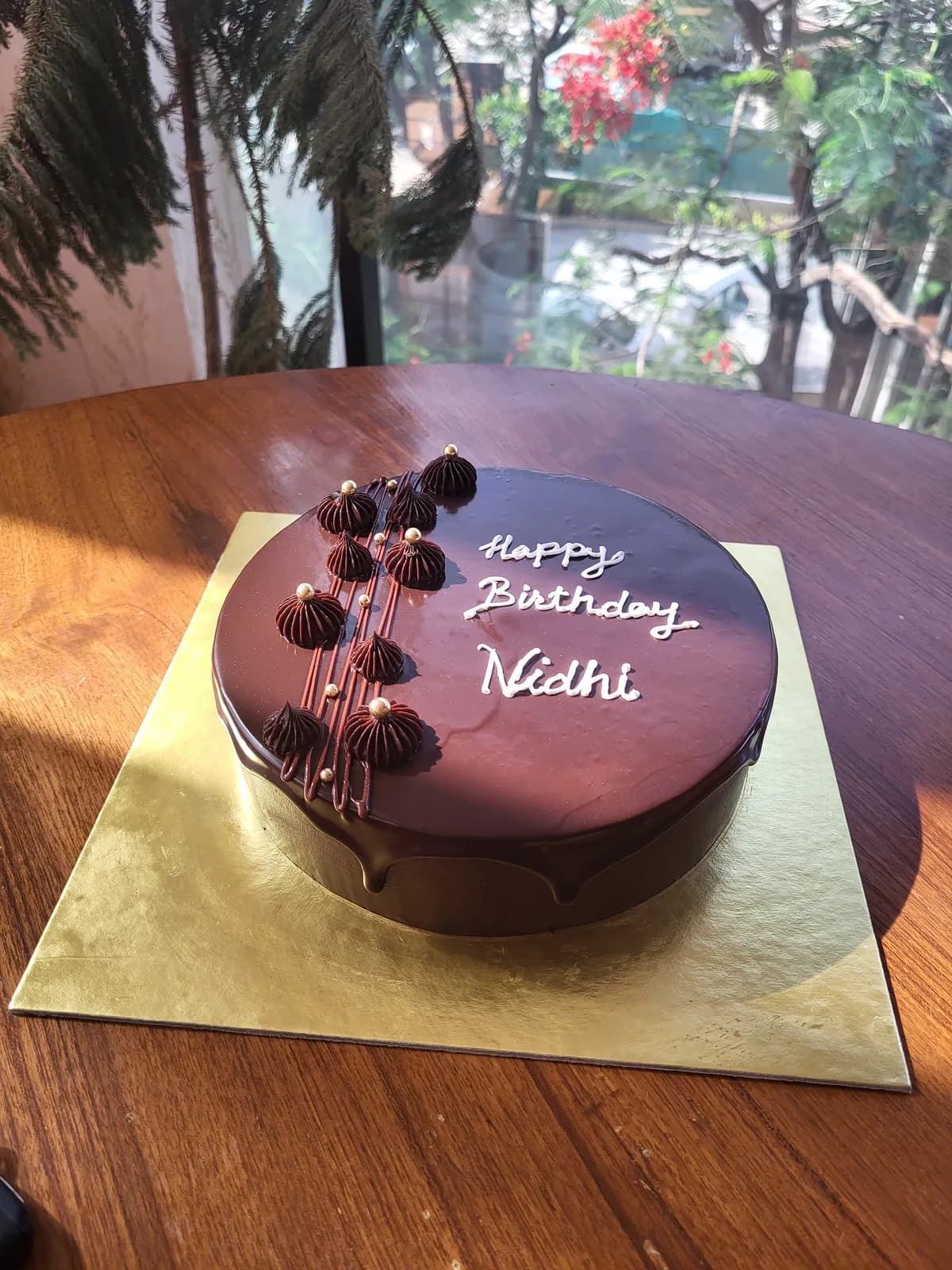 A chocolate glaze cake finished with piped rosettes, gold pearls and a hand-piped birthday message