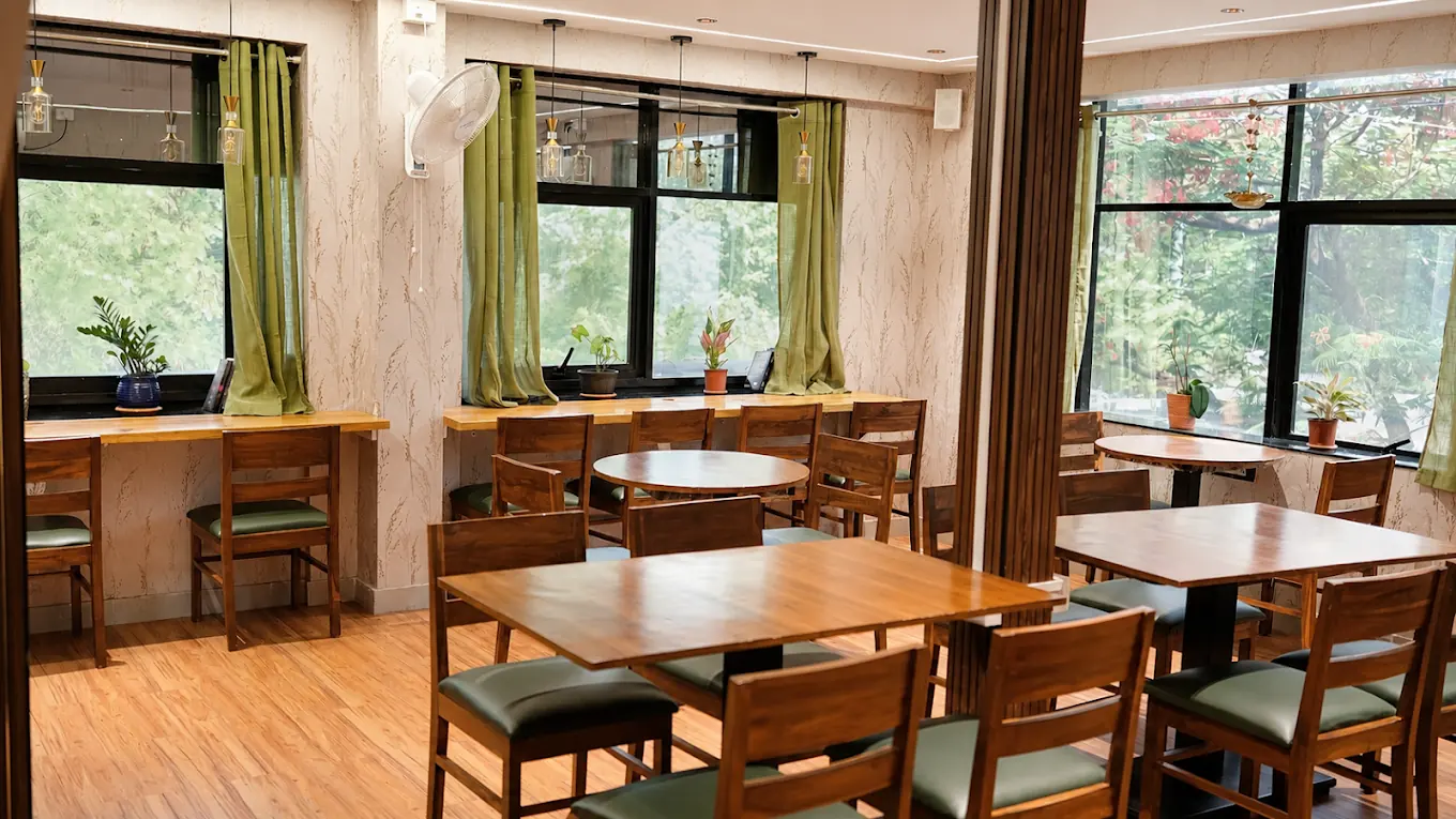 Tessori's café floor with wooden tables, green leather chairs and a window counter looking out onto trees